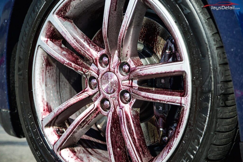 Car wheel being cleaned; red iron remover reacting with brake dust.