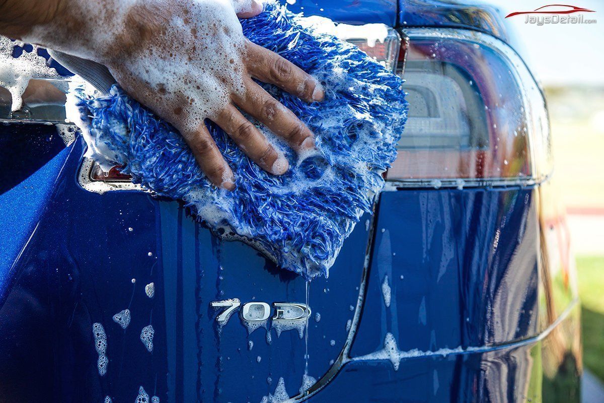 Hand washing a blue car with a soapy blue washcloth.