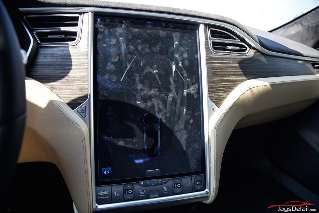 Tesla car interior with large touchscreen display, wood grain trim, and beige accents.