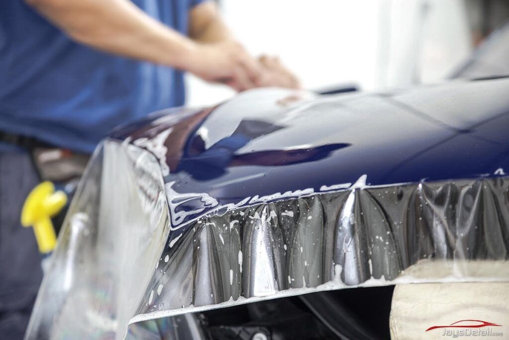 Person applying clear protective film to the hood of a blue car.