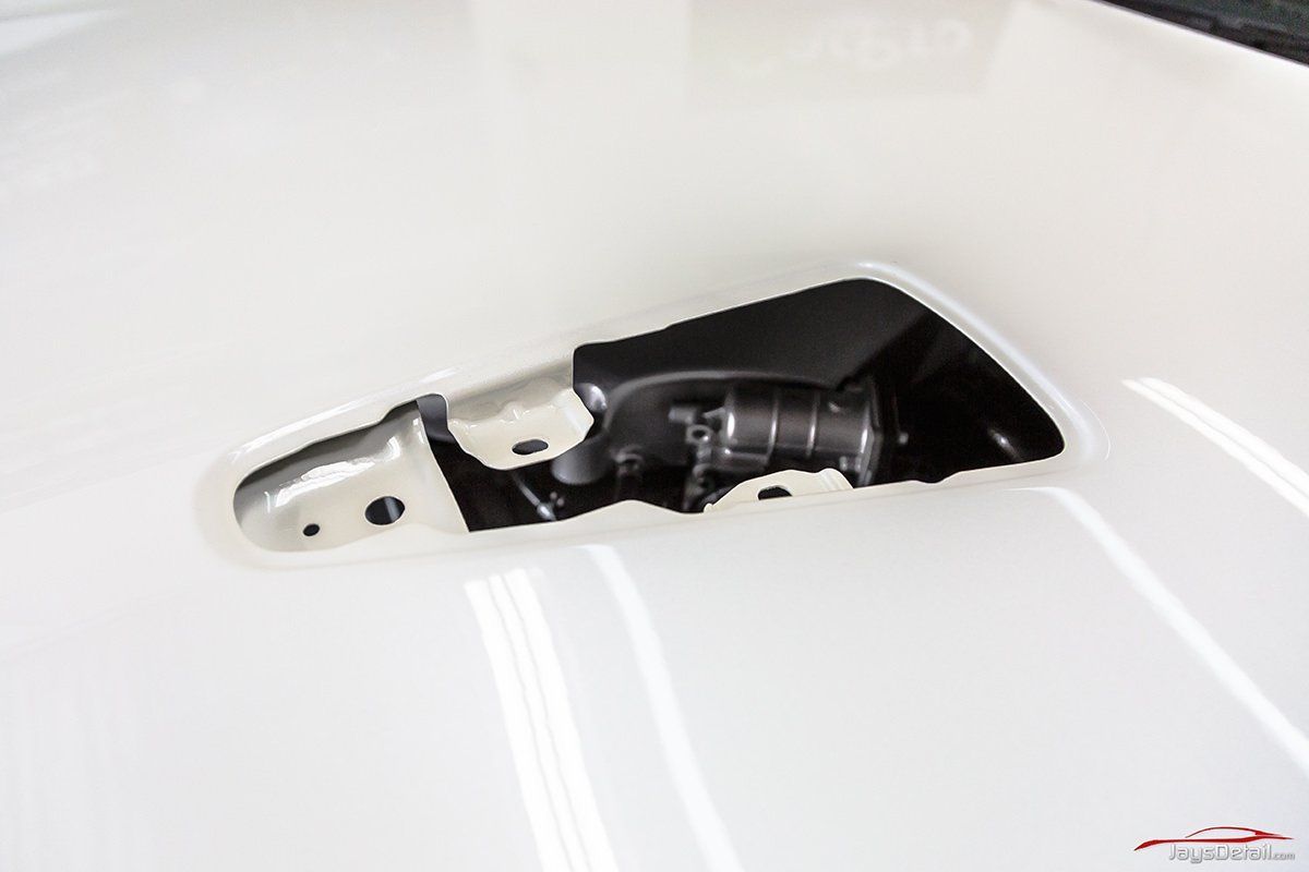 Hands applying protective film to a black car hood in a garage setting.