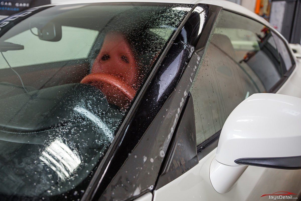 Person in a car covered in water droplets, applying tint film to the windshield.