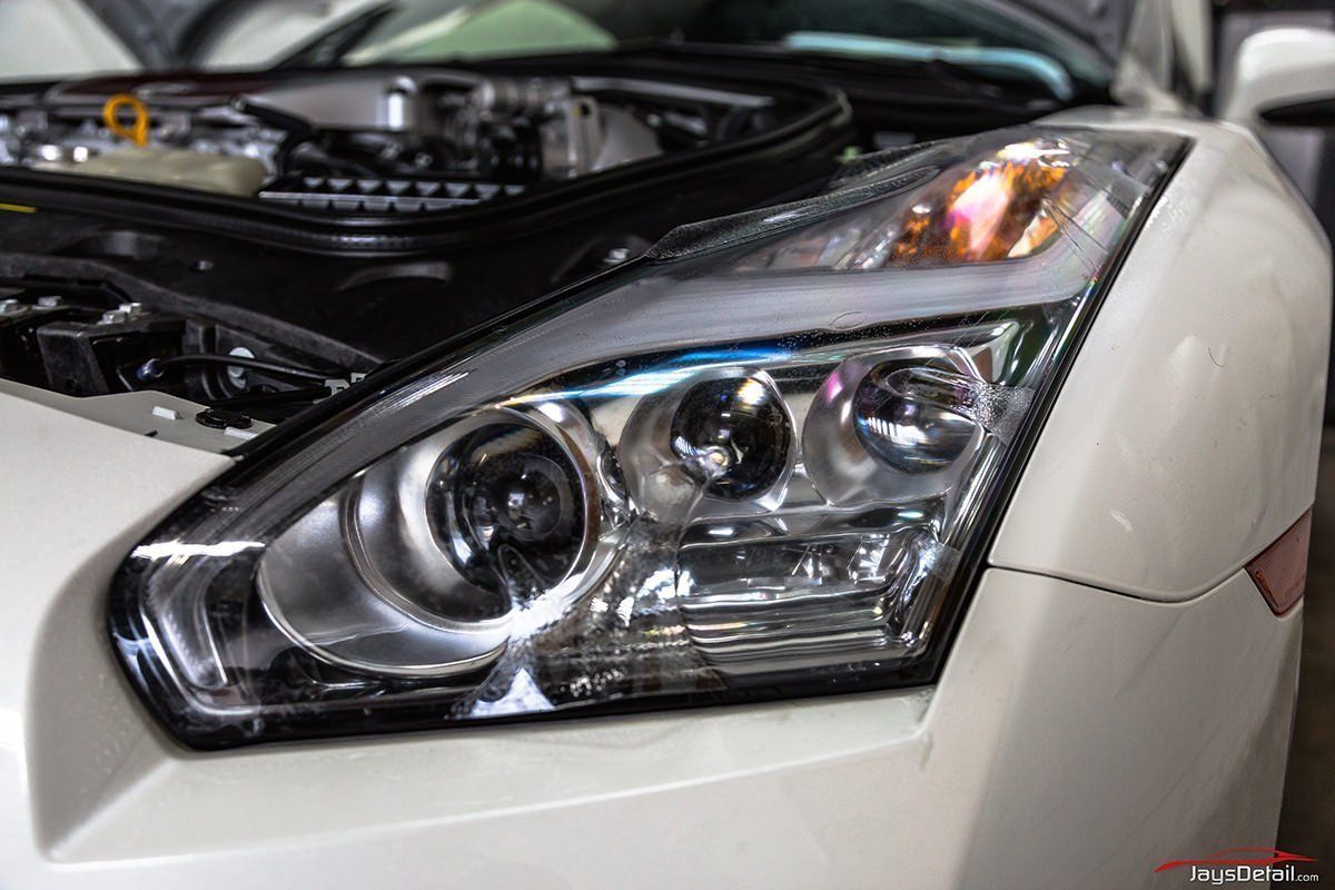 White sports car headlight with hood open, revealing engine.