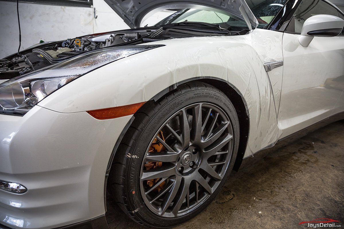 White Nissan GT-R sports car with the hood open, revealing the engine bay. The car is in a garage setting.