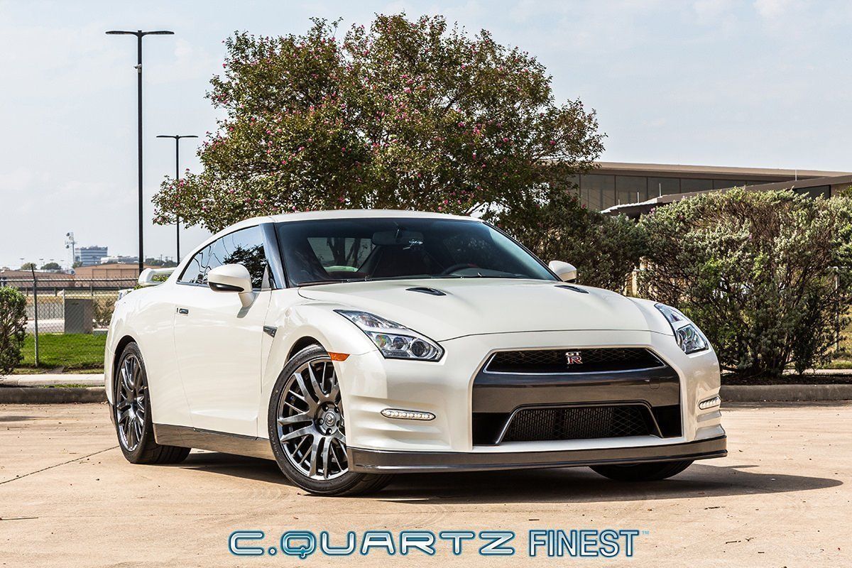 White Nissan GT-R sports car parked on gravel, with dark gray wheels, against a sunny backdrop.