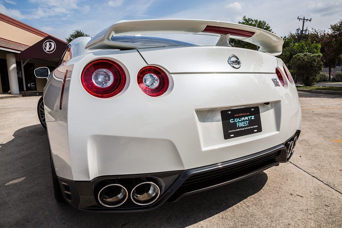 White Nissan GT-R sports car with large spoiler, dual exhaust, and red taillights parked in front of a building.