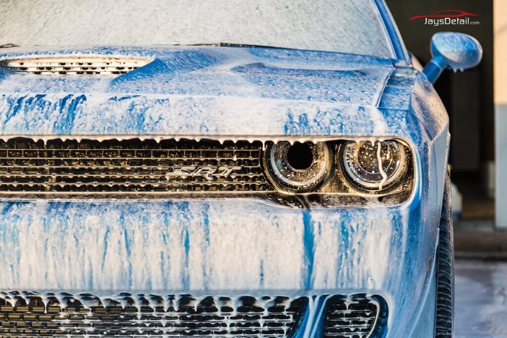 Blue Dodge Challenger covered in white foam at a car wash.