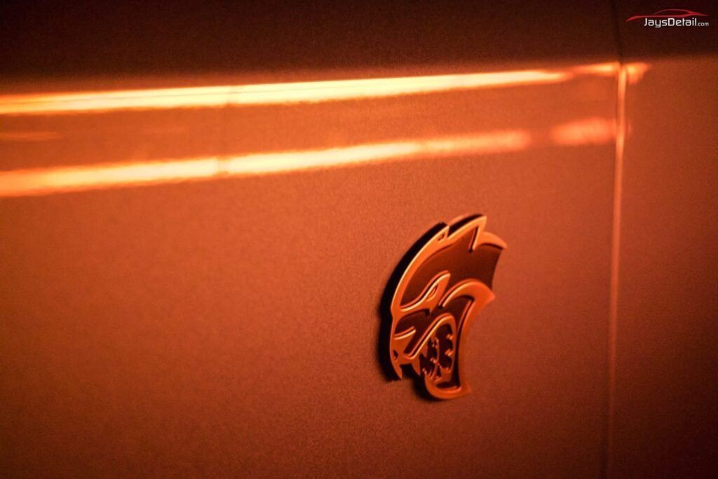 Dodge Hellcat logo on car's body, illuminated by orange light.