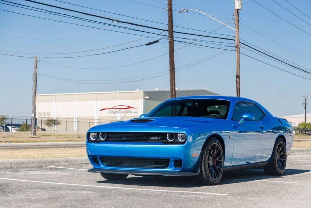 Blue Dodge Challenger sports car on a road, sunny day.