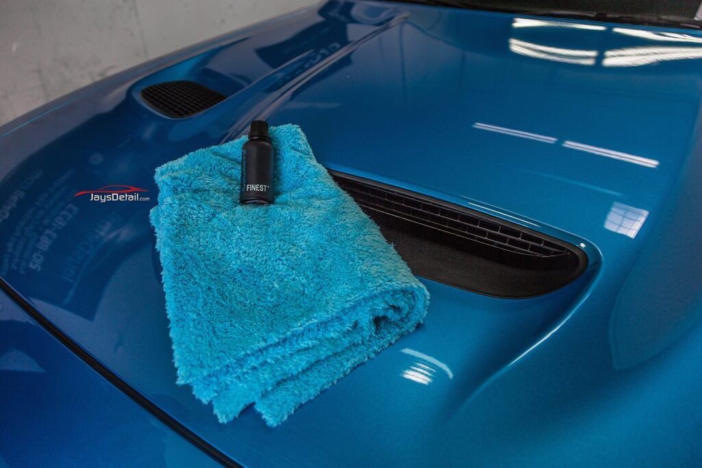 A bottle and microfiber cloth on a blue car hood.
