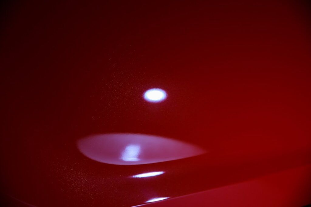 Close-up of a shiny red surface reflecting a bright white light, creating a blurry halo effect.