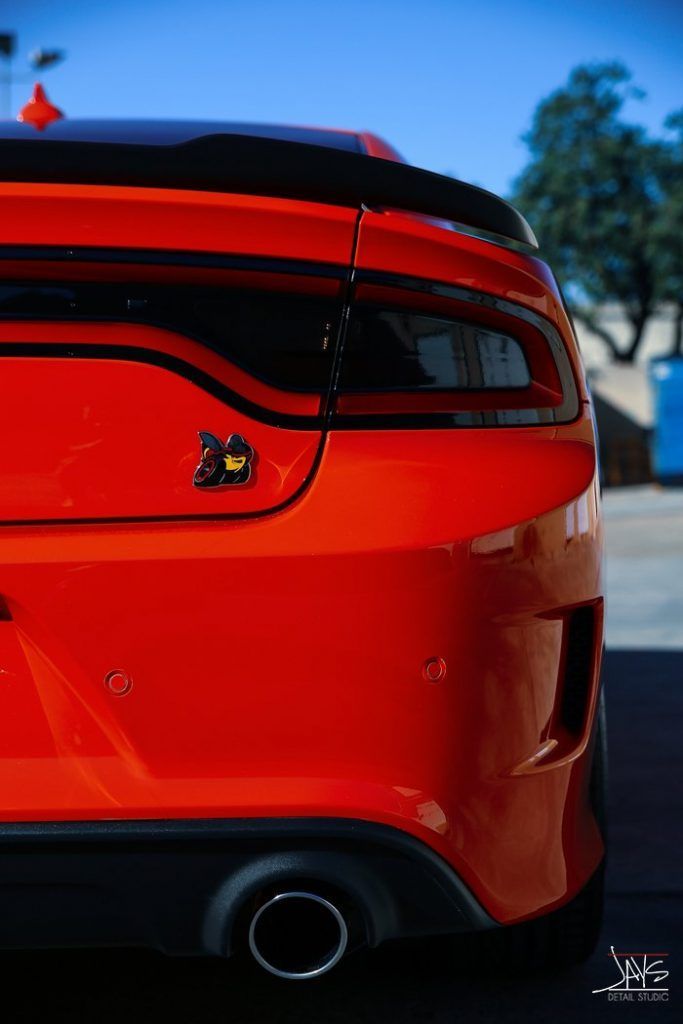 Bright red Dodge Charger's rear with black spoiler, taillight, and exhaust; parked outside.