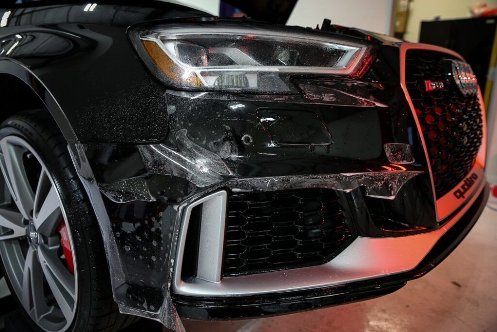 Black Audi car front bumper with protective film being applied.