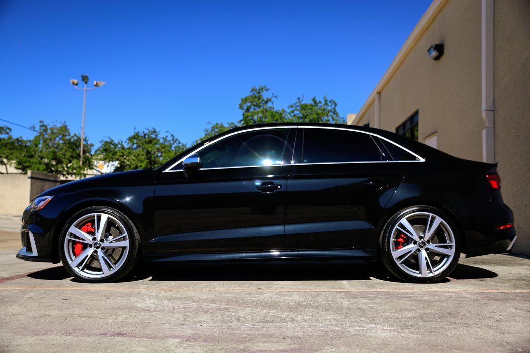Black Audi sedan parked outside on a sunny day, showing off shiny silver rims and red brake calipers.