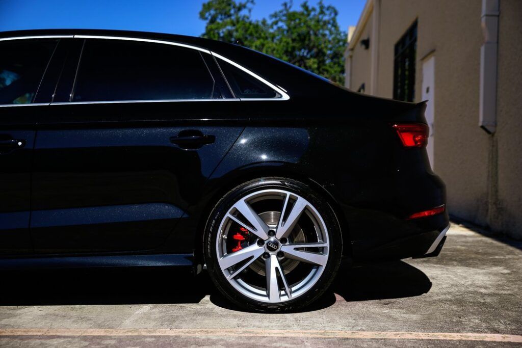 Black sedan with silver wheels and red brake calipers parked outside.