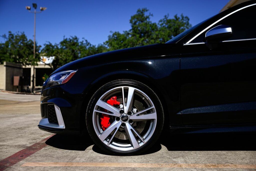 Black Audi RS3 with silver wheels and red brake calipers parked outside on a sunny day.