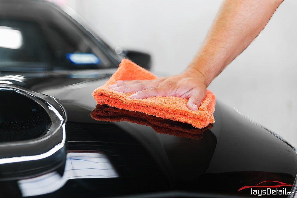 Hand polishing a black car hood with an orange microfiber cloth.