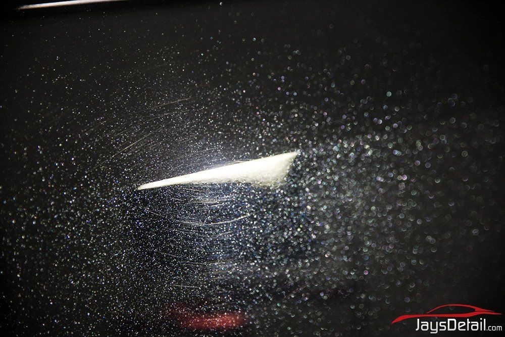 Close-up of a black car's fender, showing speckled paint and a portion of the windshield with a sticker.
