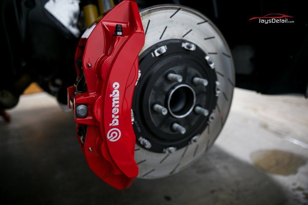 Red Brembo brake caliper on a slotted brake rotor.