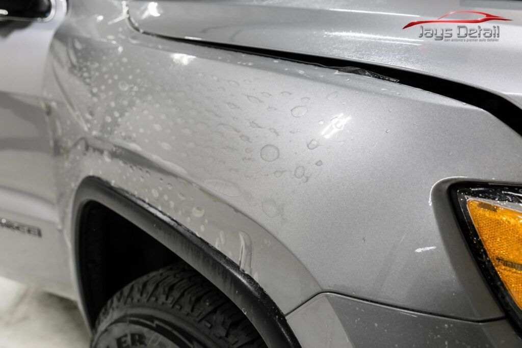 Close-up of a gray car fender with water droplets; the hood is black.