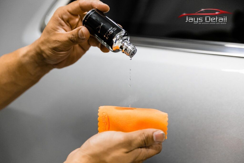 A person applies car detailing product to a sponge with product dripping.