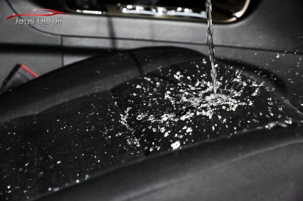 Water being poured onto a black car seat; water beads up and repels.