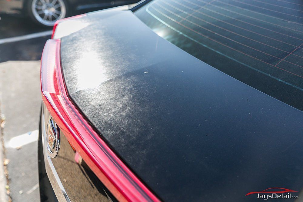Black car's trunk with damaged paint. Red light bar. Outdoor setting.