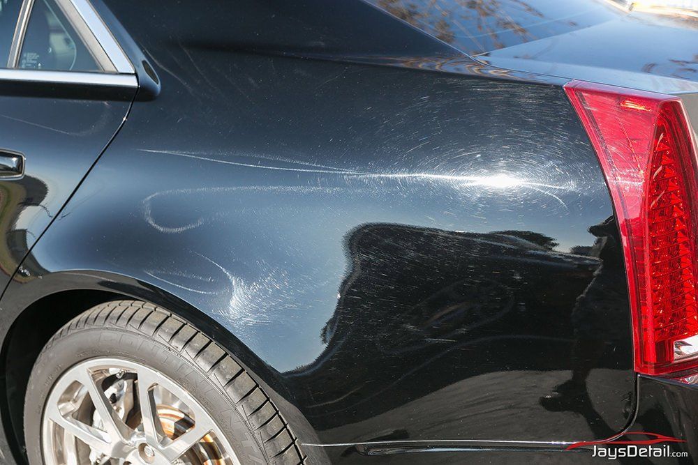 Black Cadillac car with scratches on the rear panel, reflecting sunlight.