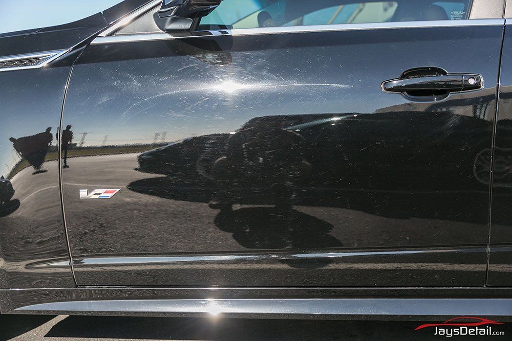Black car door reflecting other cars and a person on a sunny day.