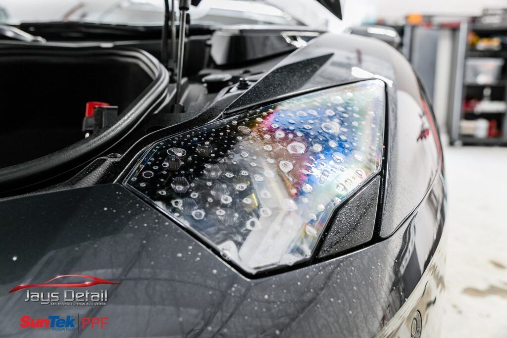 Close-up of a black Lamborghini headlight with water droplets, reflecting colors.