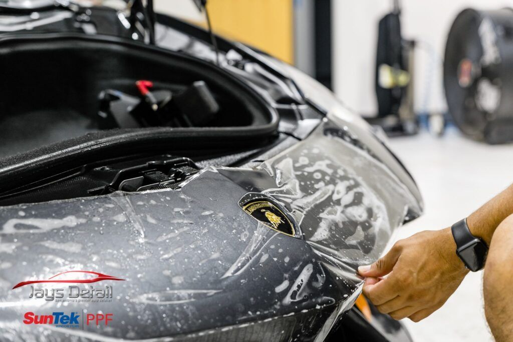Person applying protective film to a car's bumper, a SunTek PPF installation at Jay's Detail.