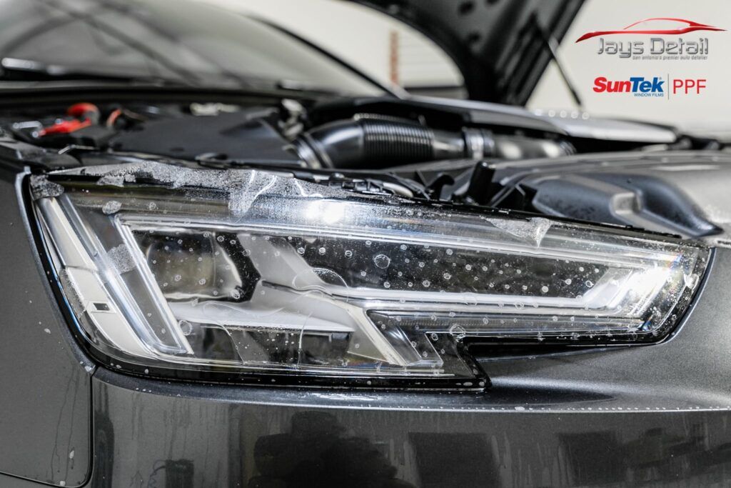 Headlight with protective film being applied on a gray car in a detail shop.