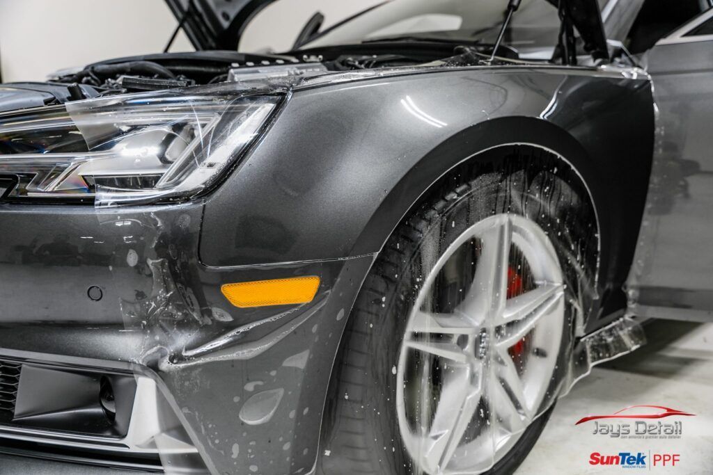 Car being detailed with protective film application. Gray car, front quarter view, wet, red brake caliper.