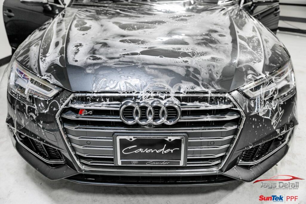 Black Audi car covered in foam. Front view, outdoors.