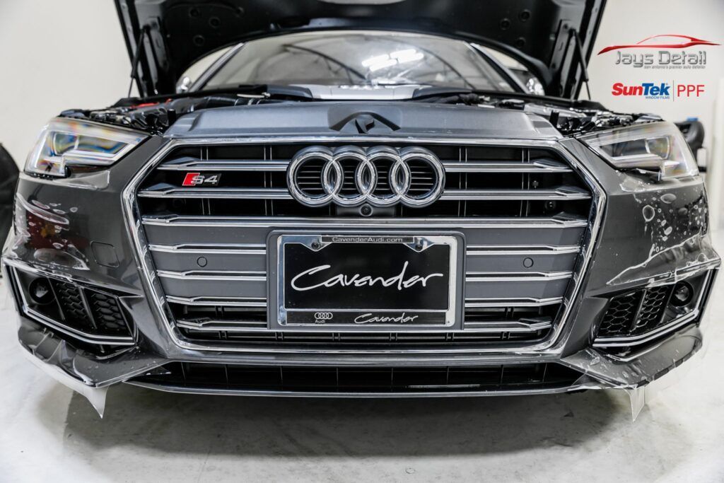 Dark gray Audi with a custom front grille and the hood open in a garage setting.