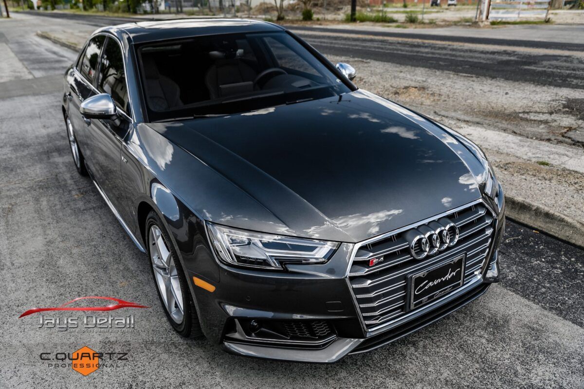 Dark gray Audi S4 sedan parked on a street with a logo in the corner.