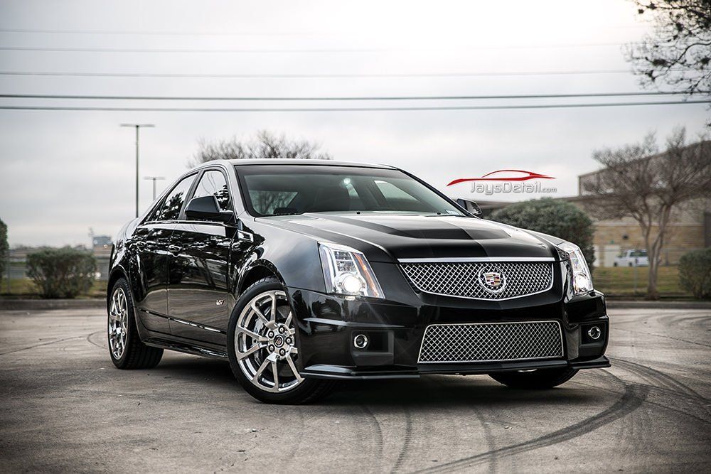 Black Cadillac CTS-V on a paved surface; front view, chrome wheels, cloudy day.
