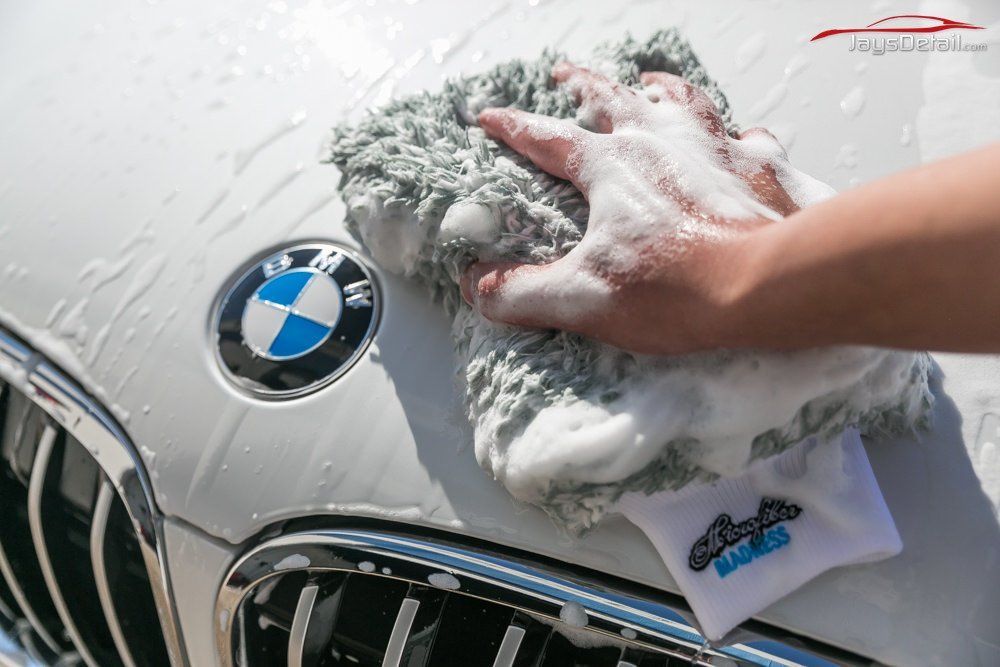 Person washing a white BMW car with a soapy gray microfiber mitt.