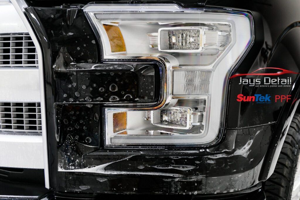 Black car headlight with protective film applied. Close-up, shiny.