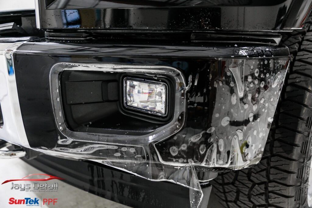 Black car bumper with protective film around a fog light.