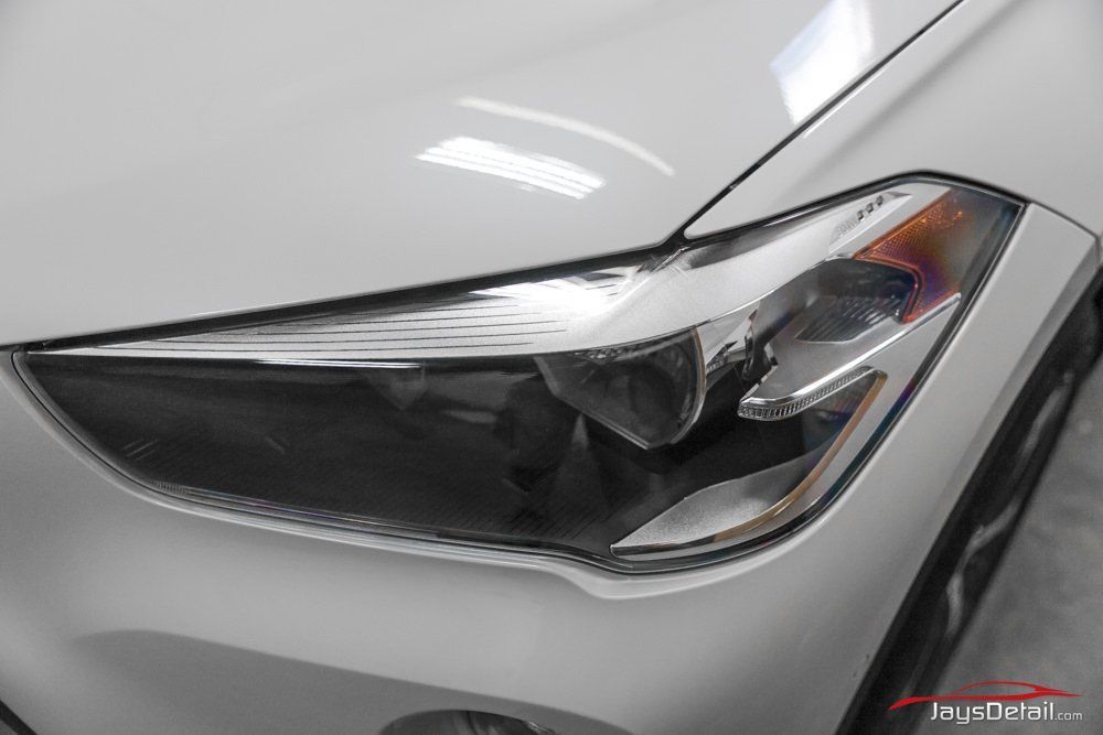 White car headlight, angled shot, part of car body visible.