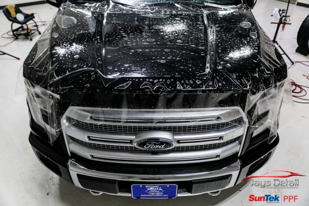 Car's front with clear protective film being applied over the black hood and silver grill.
