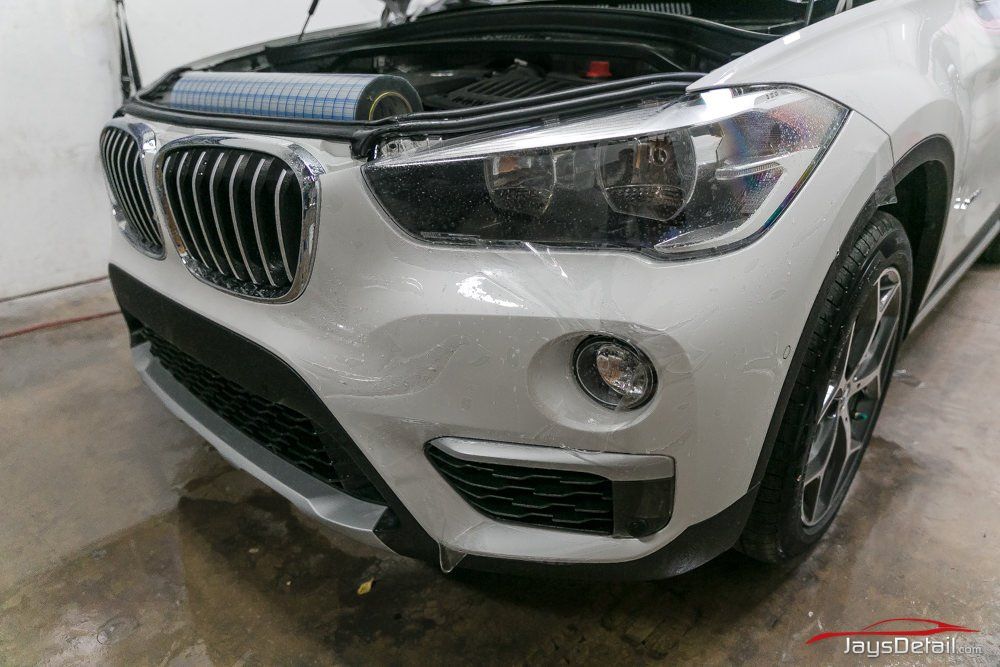 White BMW car with protective film on front bumper and headlights.