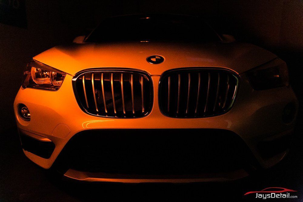Close-up of a white BMW car front, illuminated with orange light, in a dark setting.