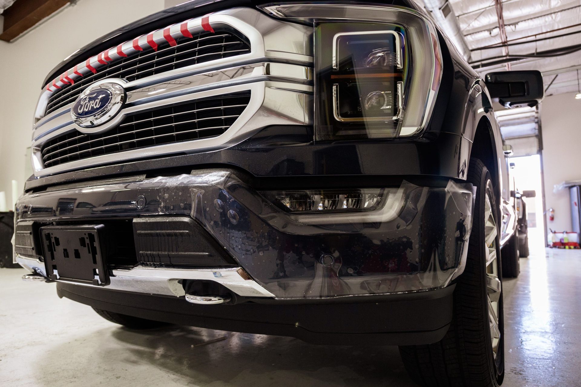 Close-up of a black Ford truck's front grill and bumper inside a garage.