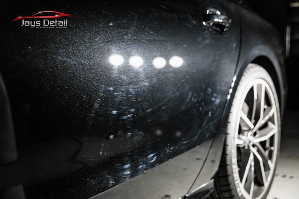 Black car door with visible swirl marks under bright lights.