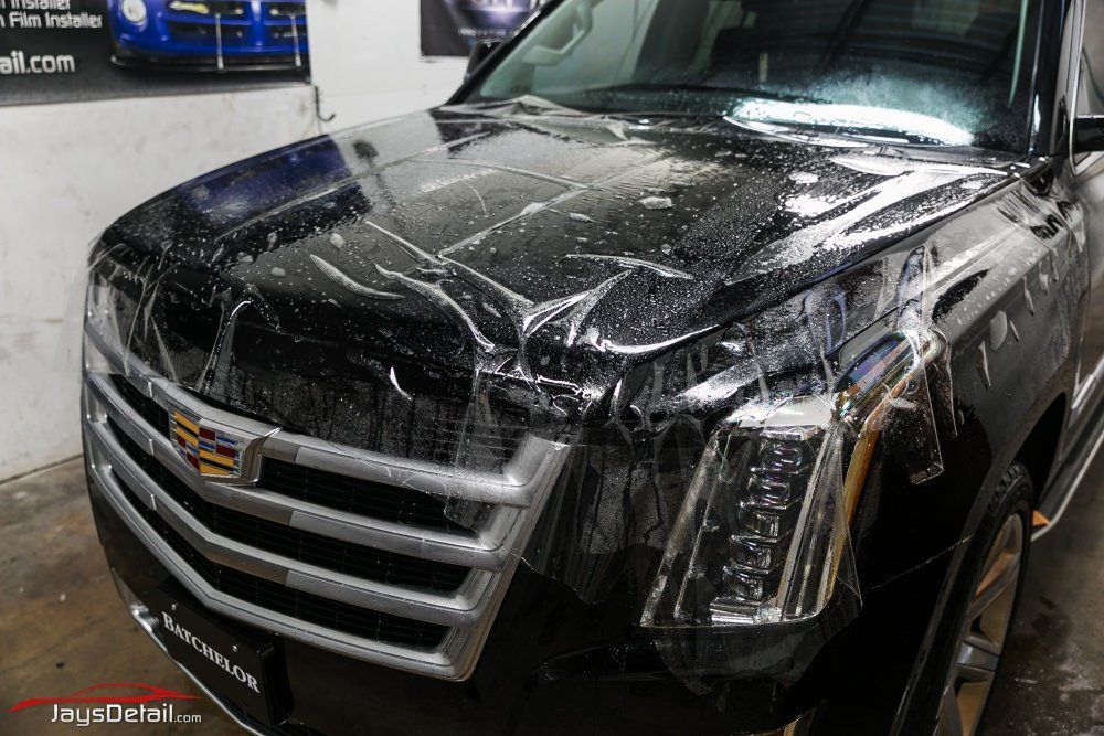 Black Cadillac SUV with clear protective film applied to the hood.