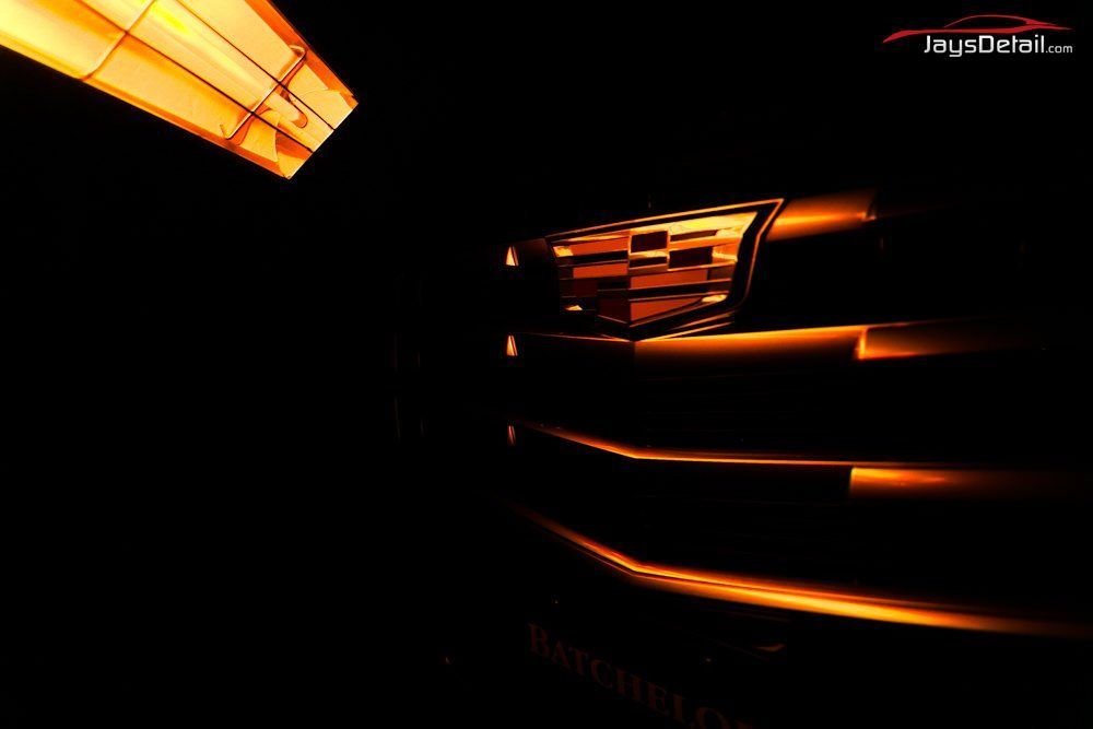 Cadillac car grille in a dark setting, highlighted with warm orange light.