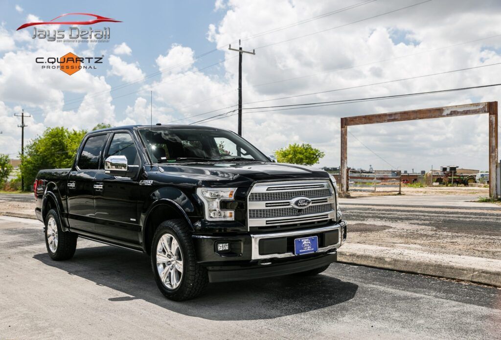 Black Ford F-150 truck parked on a road, sunny day.