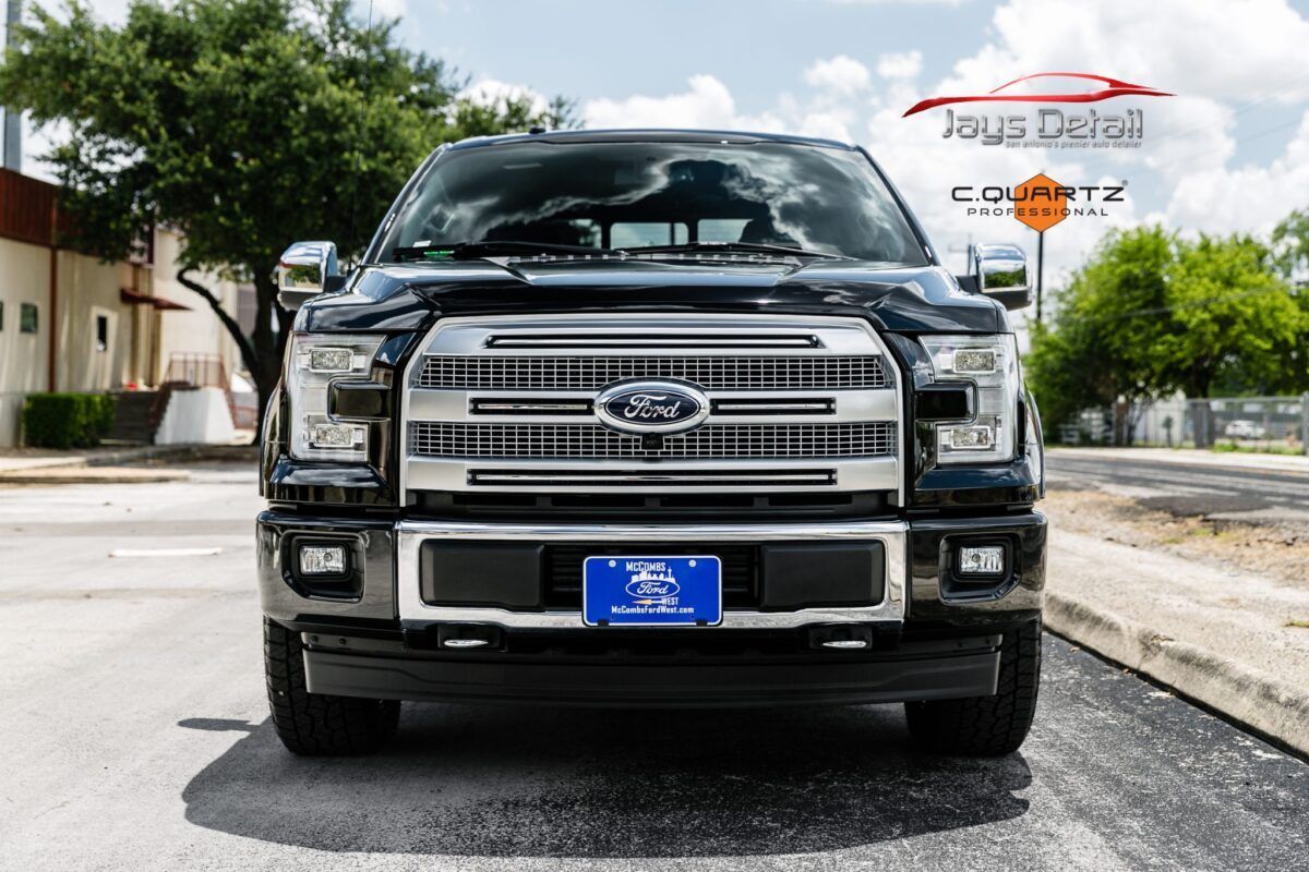 Black Ford pickup truck with chrome grill, parked on a road in front of a building.